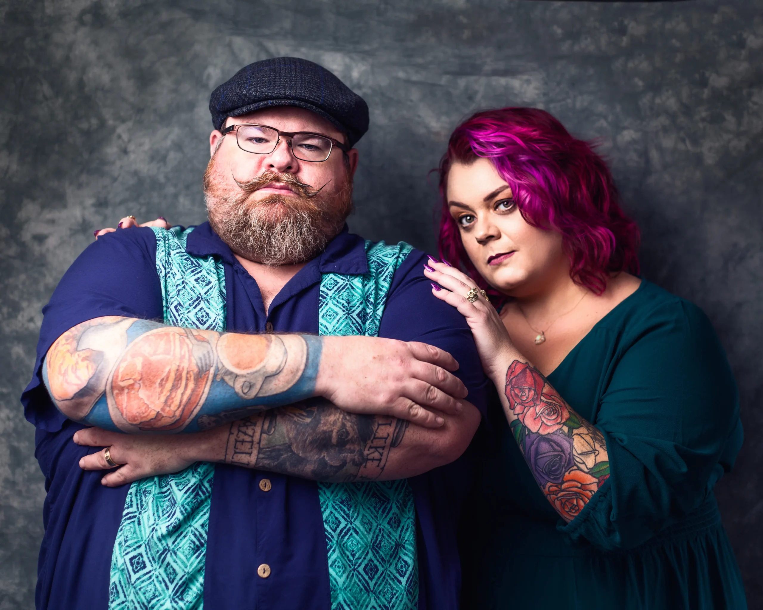 A man and woman with visible tattoos stand side by side, showcasing their unique body art and style.